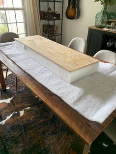 a wooden table with white cloth on it in front of a window and cowhide rug