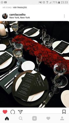 the table is set with black and white plates, silverware, and red roses