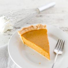 a slice of pumpkin pie on a white plate with a whisk in the background