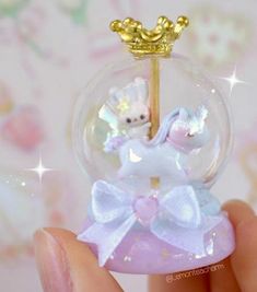 a hand holding a small glass ball with a teddy bear in it and a gold crown on top