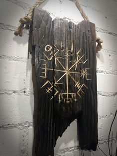 a piece of wood with writing on it hanging from a rope in front of a white brick wall