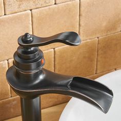 a black faucet sitting on top of a white sink next to a brown tiled wall