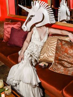 a woman sitting on top of a couch in front of a mirror wearing a paper horse mask