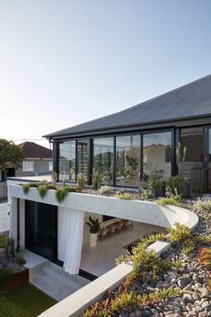 a modern house with large windows and plants growing on the outside wall, along with graveled walkways