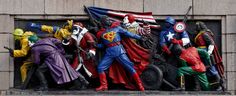 statues of people dressed as superheros and clowns are lined up on the side of a building