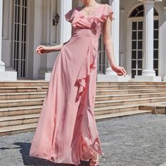 a woman in a long pink dress is standing on the steps outside an old building