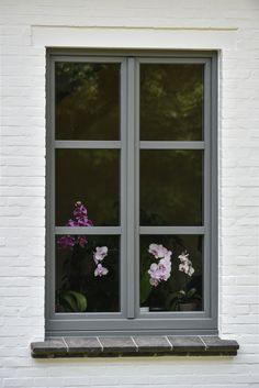 flowers are in the window sill and behind them is a white brick building with two windows