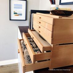 a wooden dresser with two drawers and magazines in the bottom drawer, next to a framed photograph