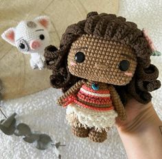 a small crocheted doll is being held up by someone's hand and another stuffed animal in the background