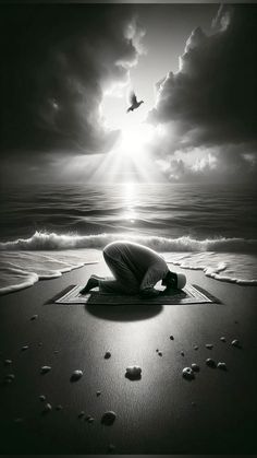 a man kneeling on top of a sandy beach under a cloudy sky next to the ocean