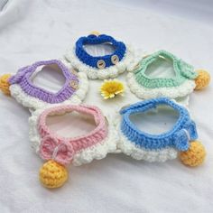 four crocheted baby bibs are arranged on a white surface with a yellow flower in the middle