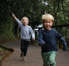 two young children running down a path in the woods, one holding his hand up