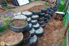 several tires stacked on top of each other in the dirt near a fence and flowers