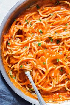 a pan filled with pasta and sauce on top of a blue cloth next to a fork