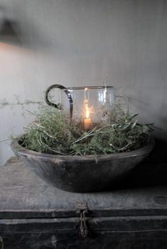 a candle is lit in a glass bowl filled with grass on top of an old trunk