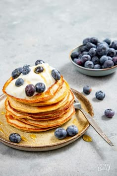 a stack of pancakes topped with blueberries and whipped cream next to a bowl of blueberries