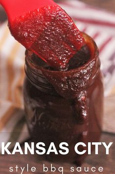 a jar filled with ketchup sitting on top of a wooden table next to a red spatula