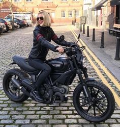 a woman sitting on top of a motorcycle in the middle of a cobblestone street