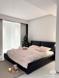 there is a large bed with pink sheets and pillows on the floor next to a small christmas tree