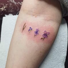 a woman's leg with three small purple flowers on the left side of her thigh