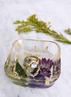 two rings sitting on top of each other in a glass container next to some flowers