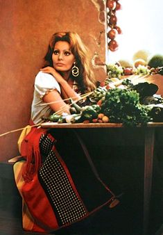 a woman sitting in front of a table filled with fruits and vegetables