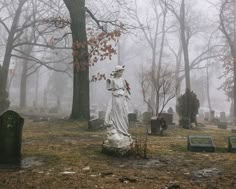 a statue in the middle of a cemetery surrounded by tombstones and trees on a foggy day