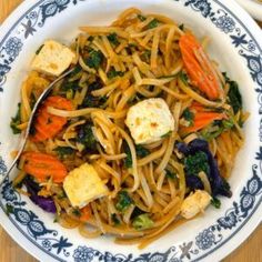 a bowl filled with noodles, carrots, and tofu pieces on top of it