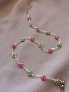 a beaded necklace with pink, green and white beads on a light pink background