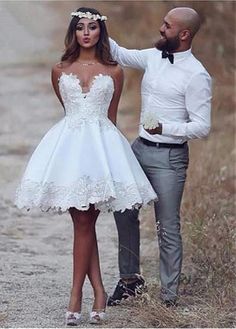 a man standing next to a woman in a white dress on a dirt road with grass