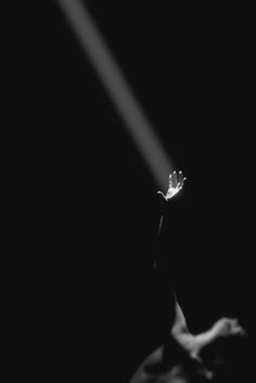 a black and white photo of a person holding a light beam in the dark with their hand