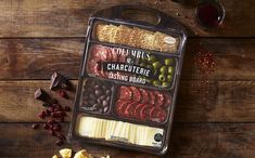 an assortment of cheeses and meats in a container on a wooden table next to crackers