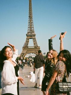 three women are standing in front of the eiffel tower, smiling and waving