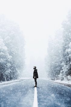 a person standing in the middle of a road on a snow covered street with trees