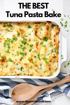 a casserole dish with cheese and parsley on the side next to a wooden spoon