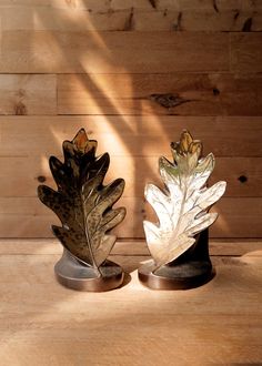 two metal leaf sculptures sitting on top of a wooden table