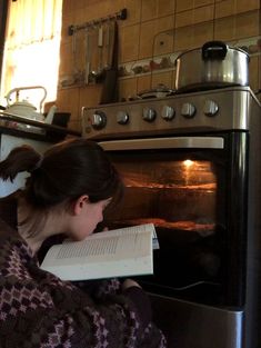 a woman reading a book in front of an oven