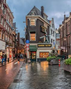 people are walking down the street in front of some buildings on a rainy day at dusk