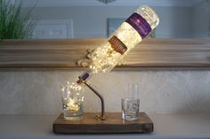 a lighted bottle lamp sitting on top of a wooden table next to two shot glasses