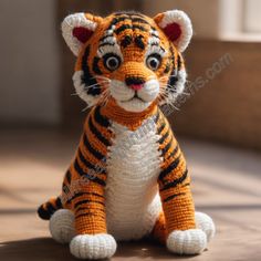 a crocheted stuffed tiger sitting on the floor with eyes wide open and one paw raised