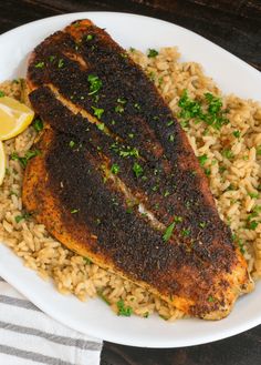 a white plate topped with fish and rice next to lemon wedges on a table