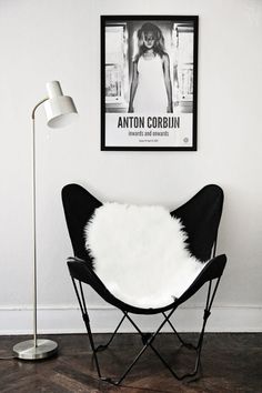 a chair with a white fur on it in front of a painting and lamp next to a floor lamp