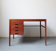 a wooden desk with three drawers on the top and one drawer at the bottom, in front of a white wall