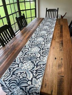 a wooden table topped with a blue and white runner next to black chairs in front of a window