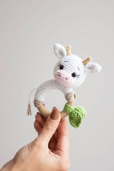 a hand holding a small crocheted cow on top of a wooden stick in front of a white wall