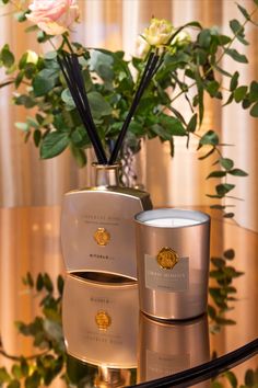 two candles on a table with flowers in the background