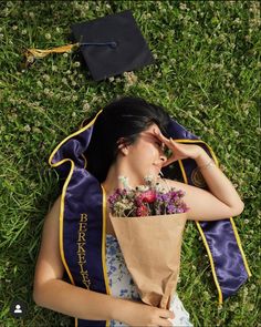 a woman laying in the grass with her graduation cap and gown over her head, holding flowers