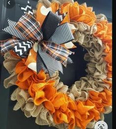 a burlock wreath with orange, black and white ribbons hanging on a door