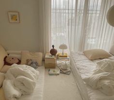 a bed room with two beds covered in white blankets and pillows next to a window