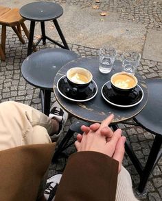 two cups of coffee sit on top of black tables with chairs around them and one person is holding their hand up to the table